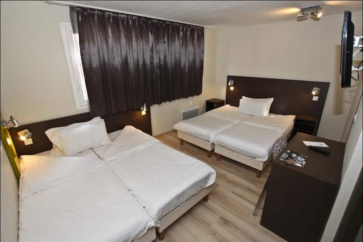 A hotel room with two beds, a small desk, a TV, and a window with curtains.