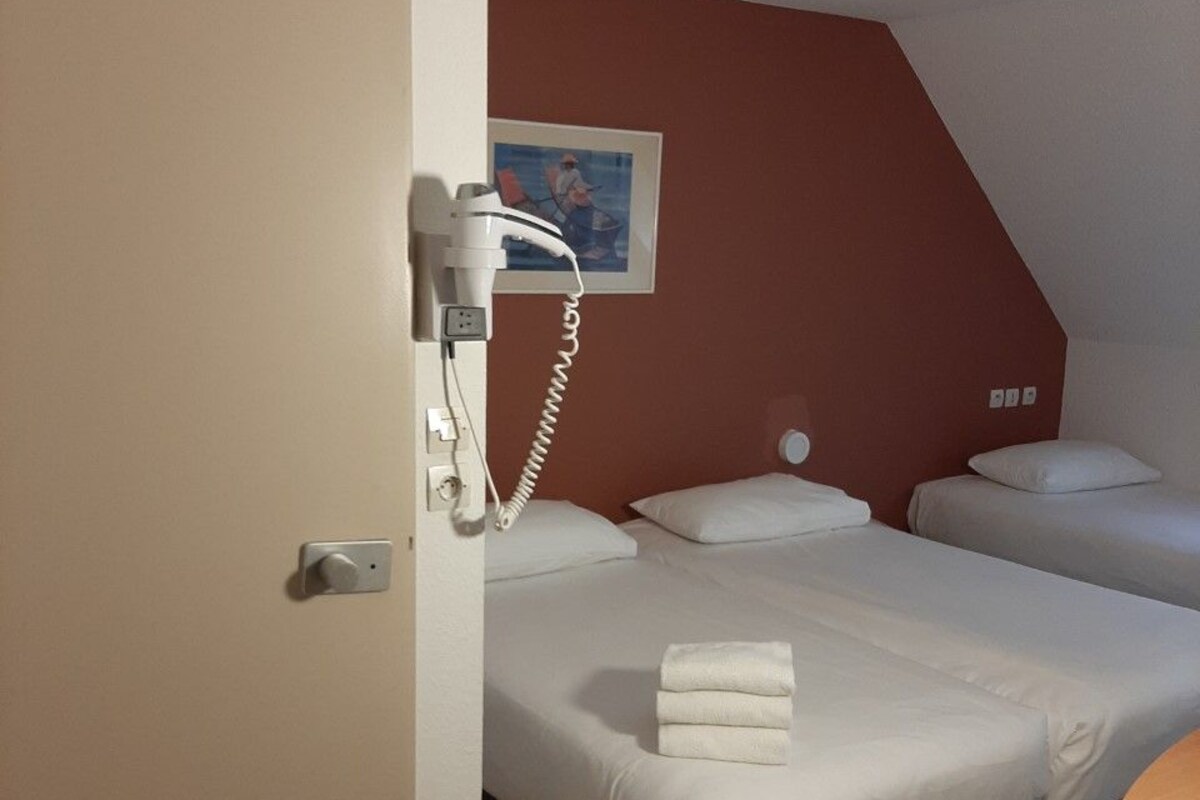 Habitación de hotel con dos camas, un secador de pelo en la pared y un cuadro colgado.
