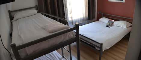 Una habitación con dos camas, una litera y una cama individual, con ventana y cortinas.