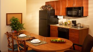 A compact kitchen with wooden cabinets, a black refrigerator, a microwave, and a dining area with a wooden table and chairs.
