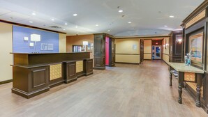 A hotel reception area with a counter, a blue wall with the hotel name, and a hallway leading to other rooms. - Holiday Inn Express Hotel & Suites Huntsville by IHG (Huntsville)