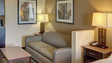 Una camera d'albergo con divano, un tavolino, una lampada, un comodino con il telefono e due quadri appesi al muro.