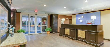 A hotel reception area with a glass door entrance, a reception desk, and a potted plant.