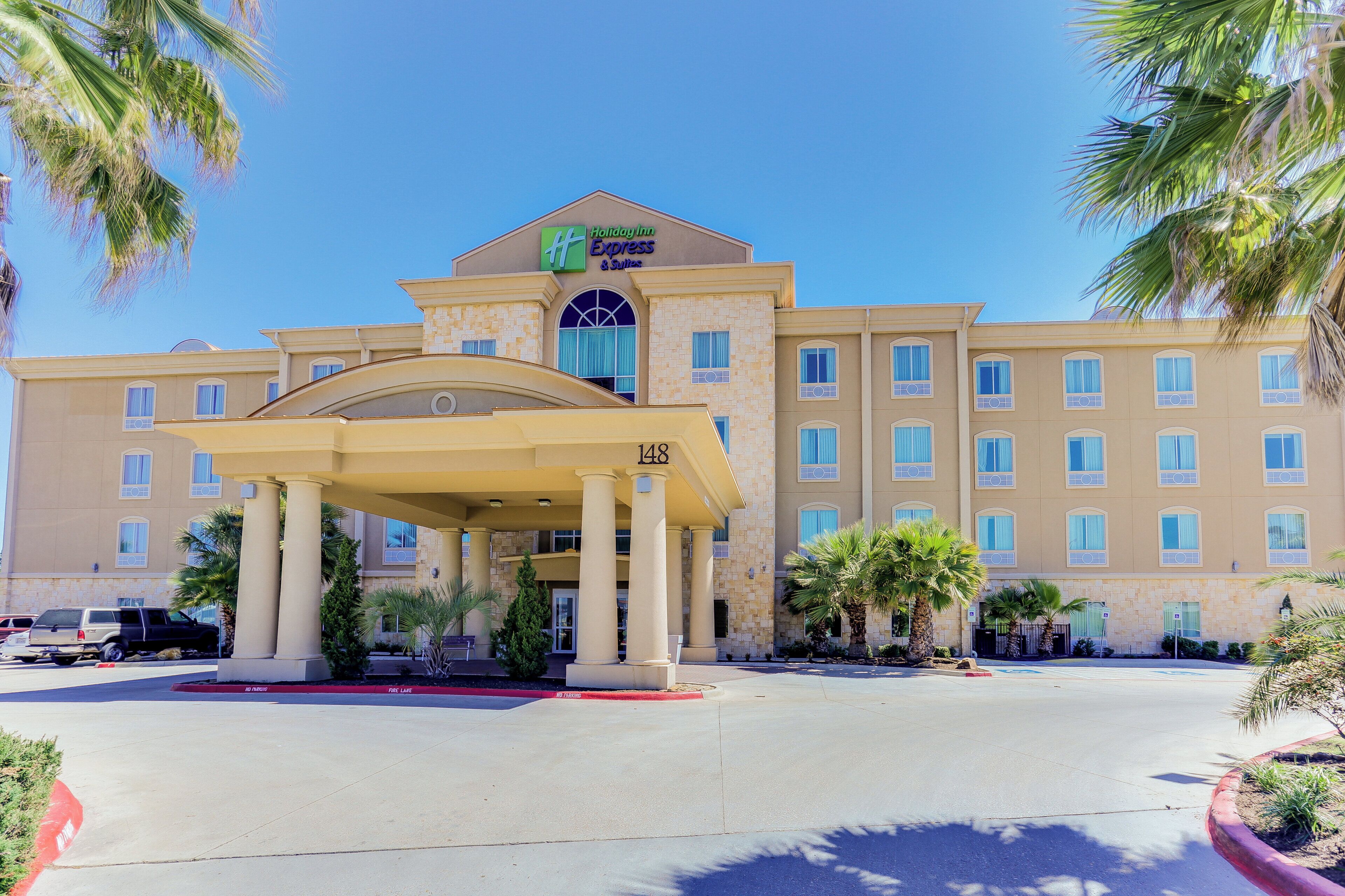 A Holiday Inn Express & Suites building with a covered entrance, multiple windows, and palm trees.