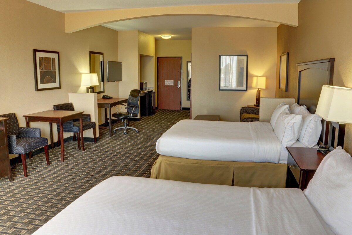 A hotel room with two beds, a desk, a chair, a TV, and a door leading to another room.