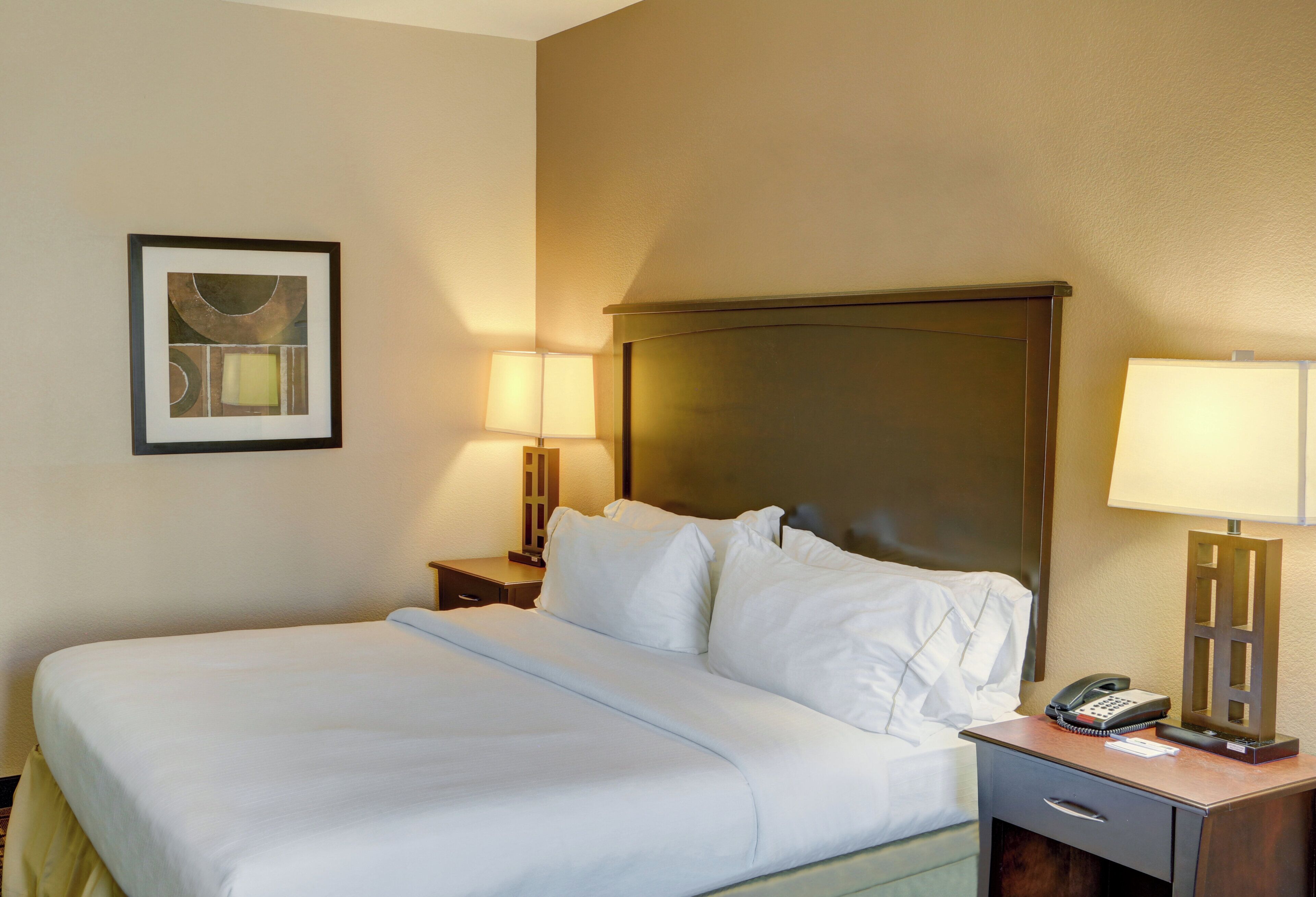A hotel room with a bed, two bedside lamps, a framed picture on the wall, and a telephone on the nightstand.