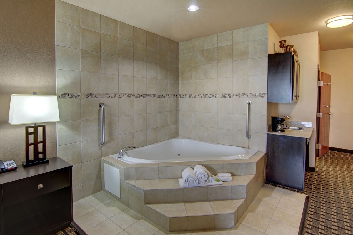 A modern bathroom with a large bathtub, a small sink, and a toilet. There are towels on the steps leading to the bathtub.