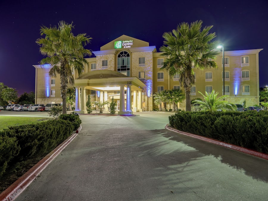 A Holiday Inn Express & Suites hotel with a central entrance, palm trees, and a parking lot.