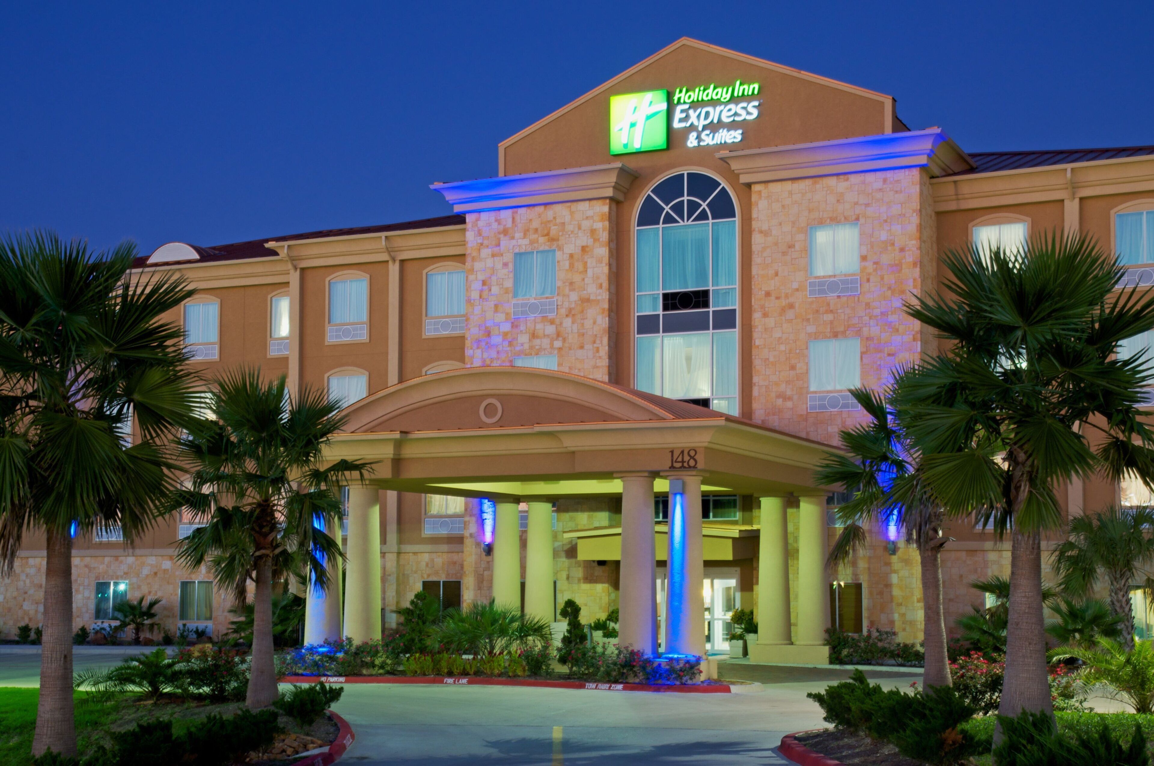 A Holiday Inn Express & Suites hotel with a covered entrance, palm trees, and a fire lane.