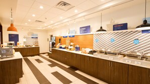 A modern hotel kitchen with a buffet setup, including labeled food stations and a patterned backsplash. - Holiday Inn Express Hotel & Suites Bay City by IHG (Bay City)