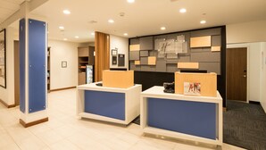 A reception area with two blue and white reception desks, a wall-mounted clock, and a door to the right. - Holiday Inn Express Hotel & Suites Bay City by IHG (Bay City)