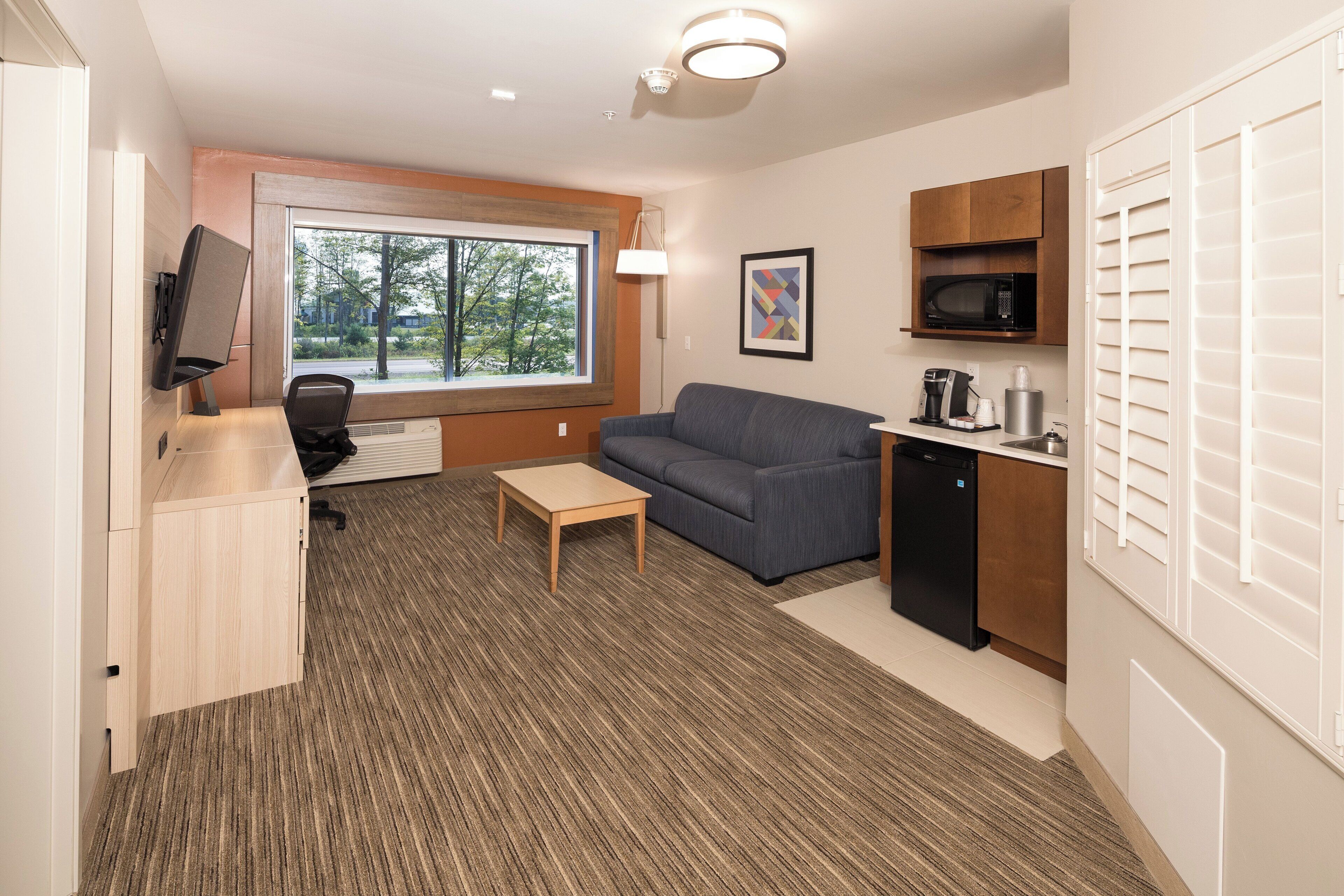 A compact living space with a sofa, a small table, a kitchenette, and a television.