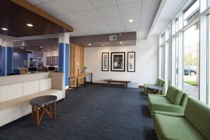 A modern lounge area with seating, a reception desk, and artwork on the walls. - Holiday Inn Express Hotel & Suites Bay City by IHG (Bay City)