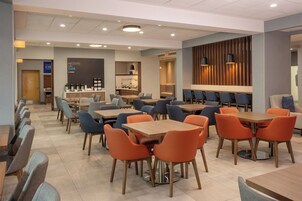 Una cafetería moderna con varias mesas y sillas, una estación de café y un área de estar con un panel de pared de madera.