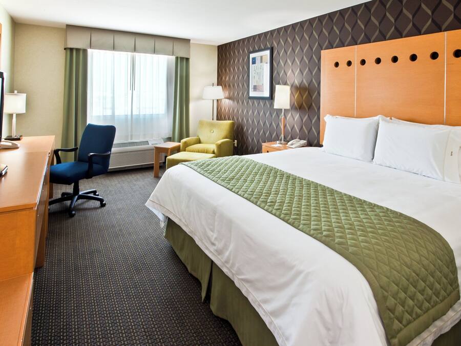 A hotel room with a bed, a desk, a chair, a TV, and a window with curtains.