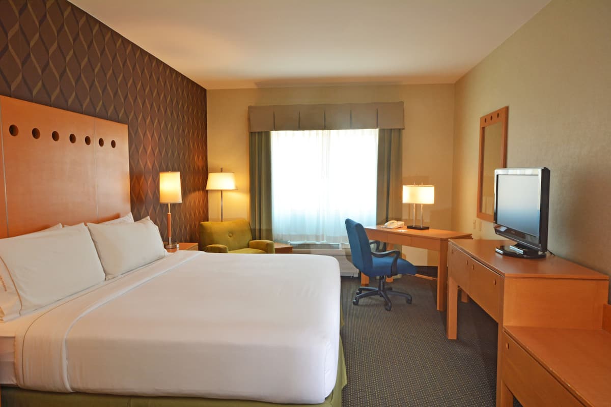 A hotel room with a large bed, a desk with a computer, a chair, and a television.