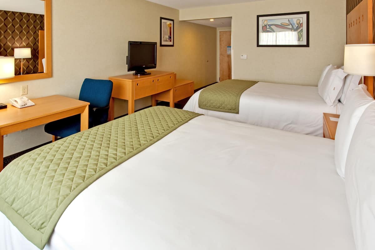 A hotel room with two beds, a desk, a chair, a television, and a mirror.