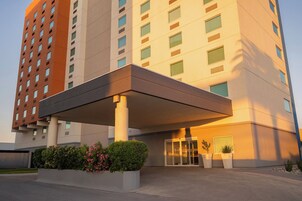 Una entrada de hotel moderna con acceso cubierto, puerta de cristal y plantas en macetas.