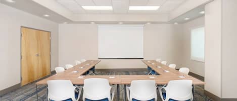 A conference room with a long table, six chairs, a projector screen, and a door.