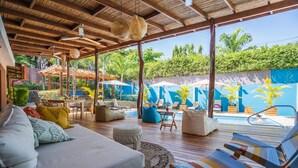 A covered outdoor seating area with a pool, wooden deck, and lounge chairs. - Hotel Arco Iris (Tamarindo)