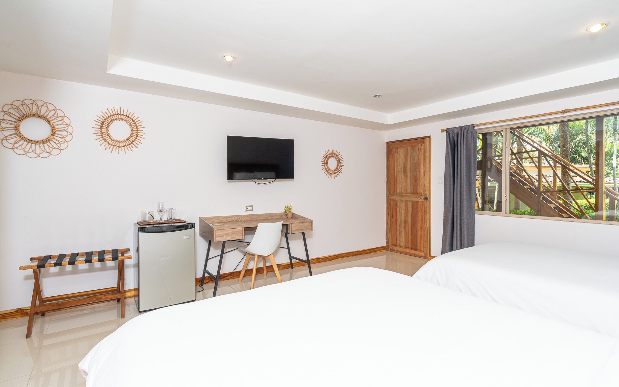 Une chambre d’hôtel avec deux lits, un bureau avec une chaise, une télévision et une porte en bois.