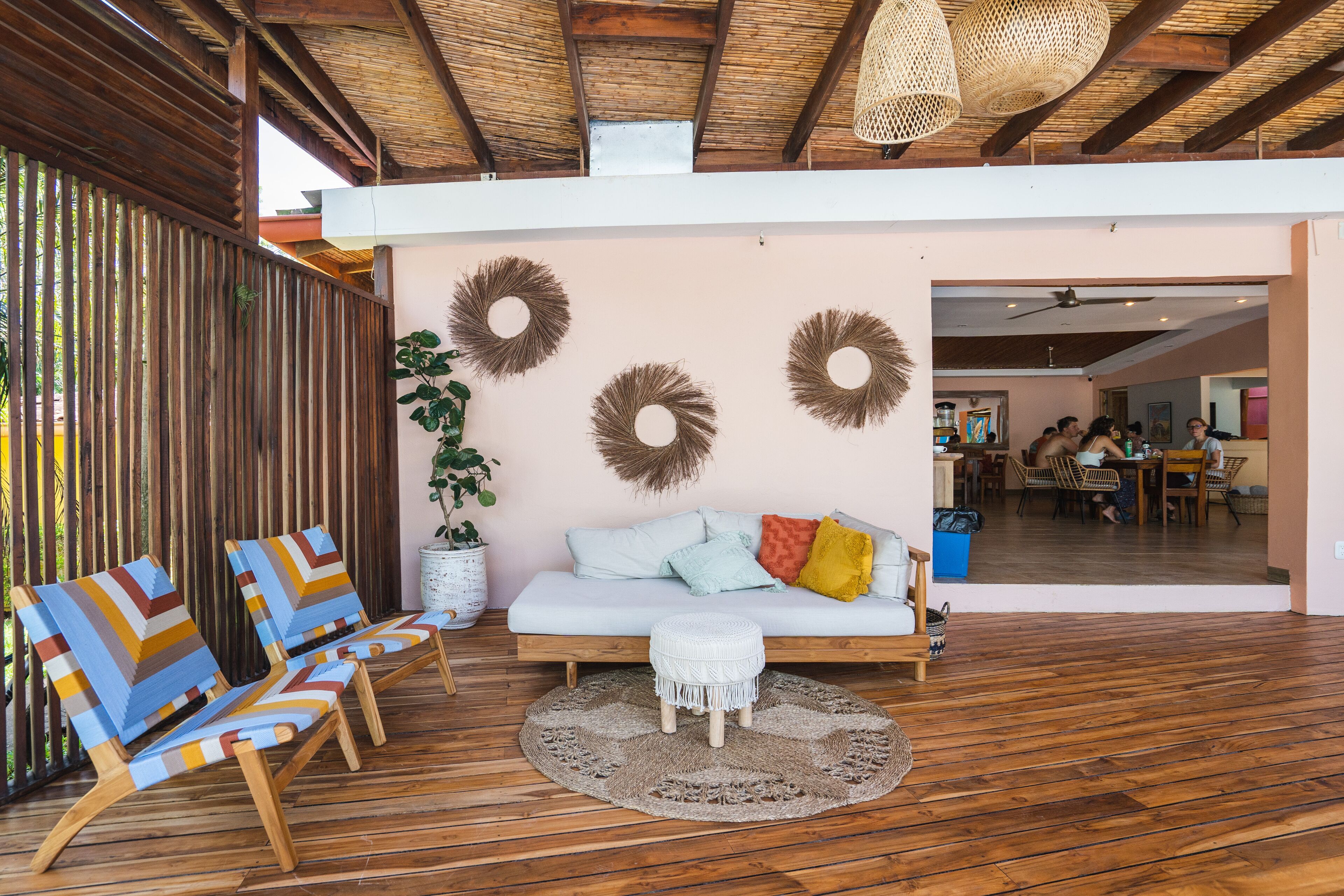 Una habitación con suelo de madera, un sofá blanco con cojines coloridos, un tapete redondo y una partición de madera con listones verticales.
