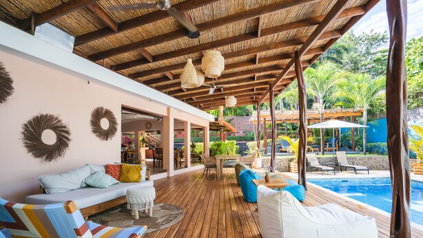 A wooden deck with a pool, outdoor seating, and a covered area with hanging lights. - Hotel Arco Iris (Tamarindo)