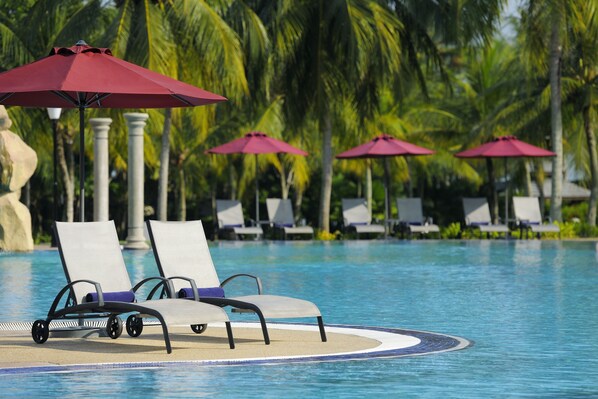 Un área de piscina con sillones reclinables y sombrillas rojas.