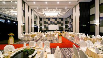A banquet hall with round tables, white chairs, and a red carpet.