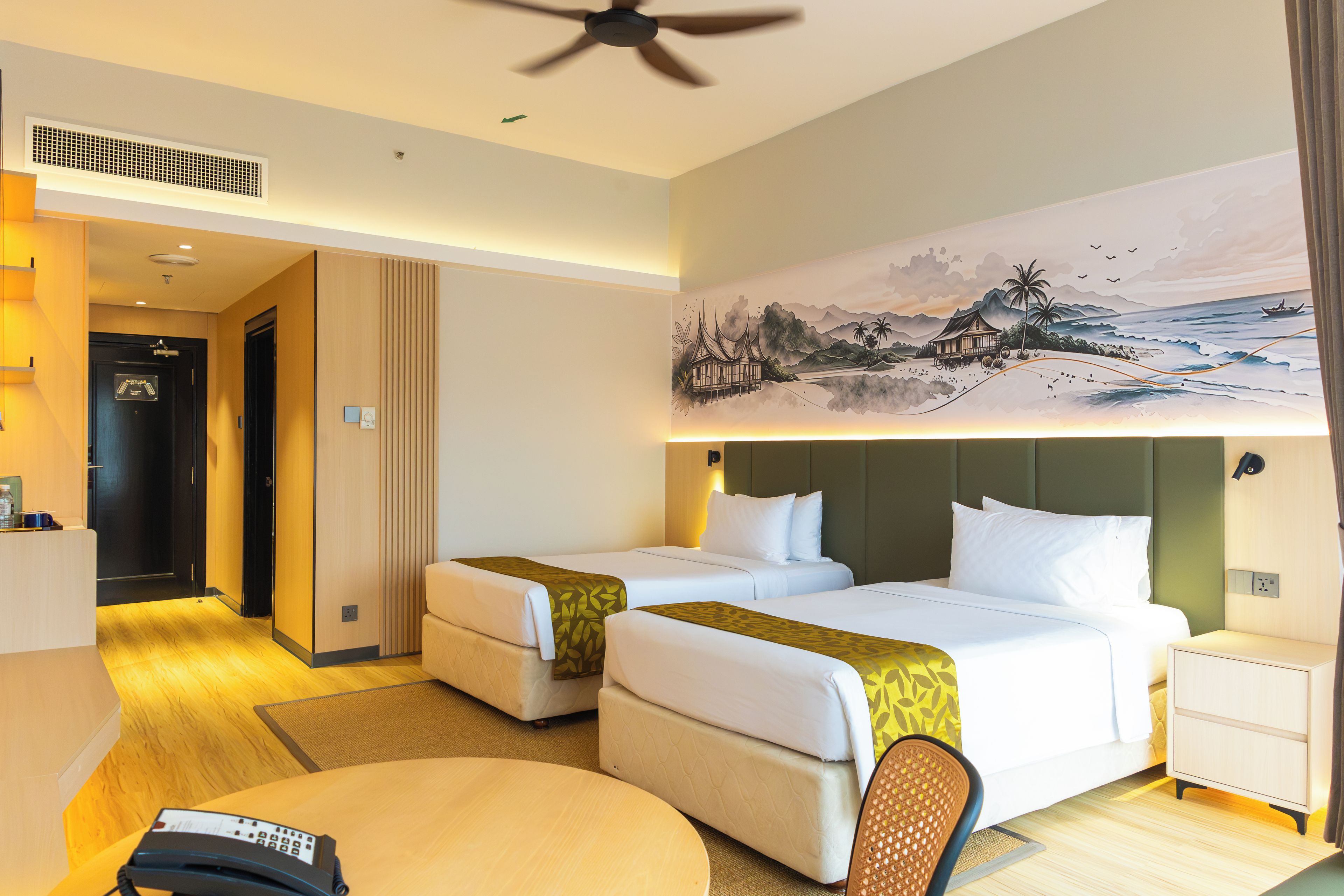 Une chambre d’hôtel avec deux lits, un bureau, une chaise, un tableau et un ventilateur de plafond.