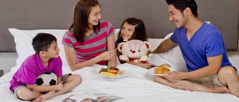 Una familia de cuatro personas en un dormitorio con una cama, almohadas y una revista sobre la cama.