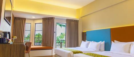 A hotel room with two beds, a desk, a chair, and a balcony with curtains.