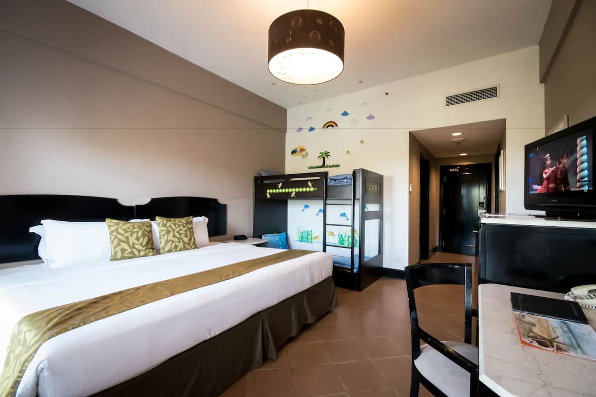 A hotel room with a large bed, a television, a desk with a chair, and a refrigerator.