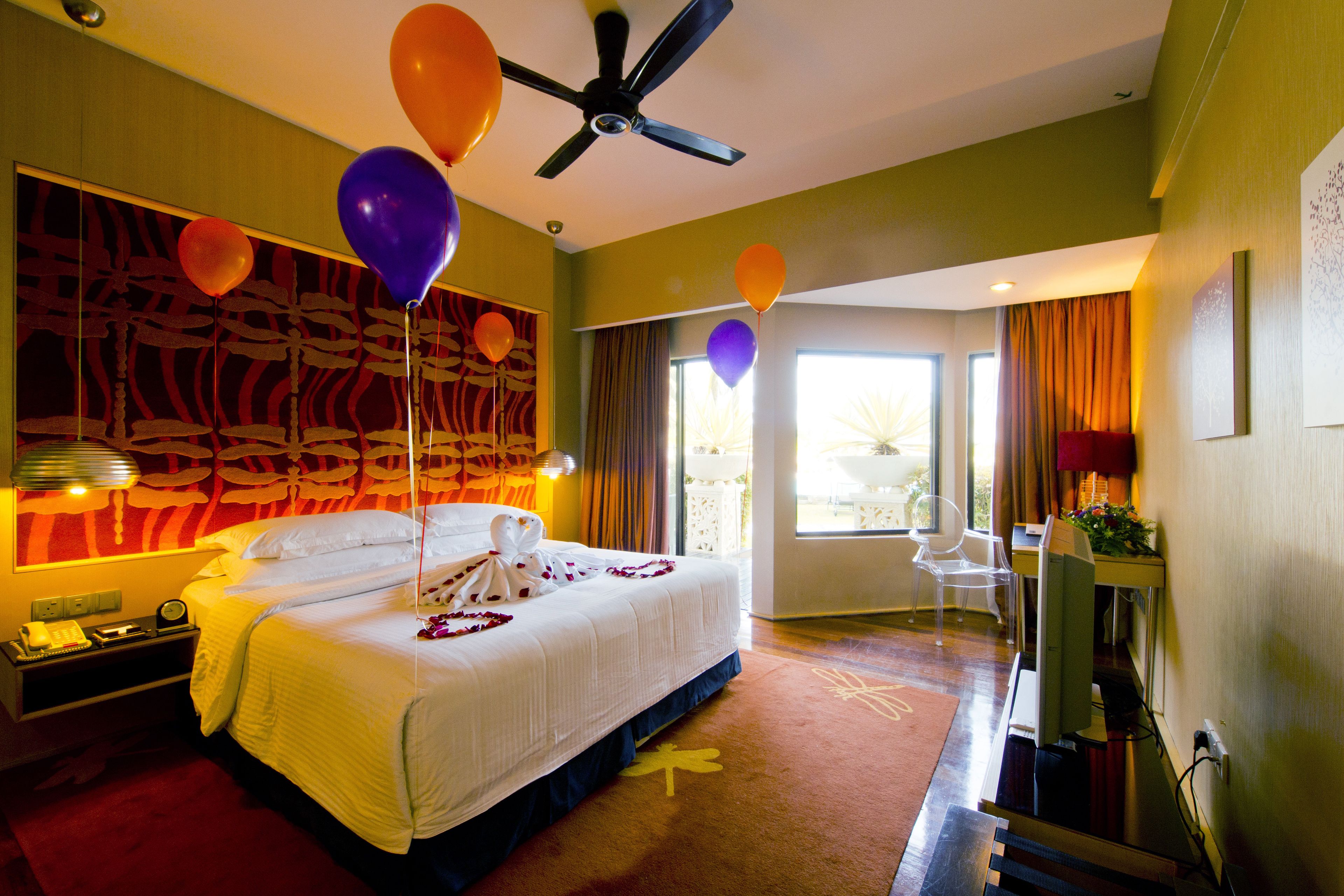 A hotel room with a bed, a desk, a chair, a ceiling fan, and balloons.