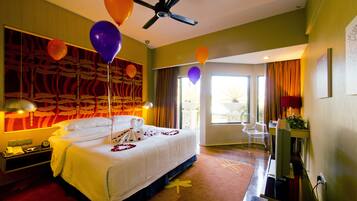 A hotel room with a bed, a desk, a chair, a ceiling fan, and balloons.