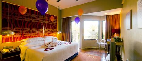 A hotel room with a bed, a desk, a chair, a ceiling fan, and balloons.