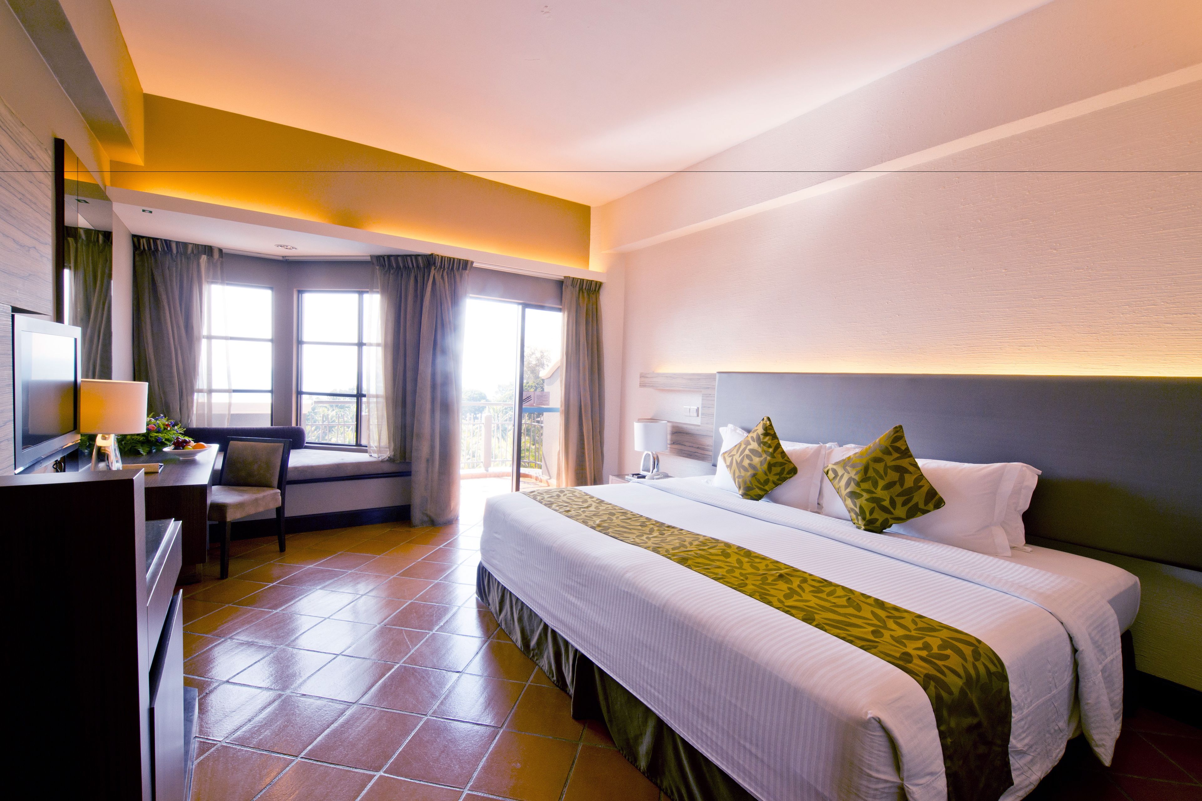 A hotel room with a large bed, a desk with a chair, a TV, and a window with curtains.