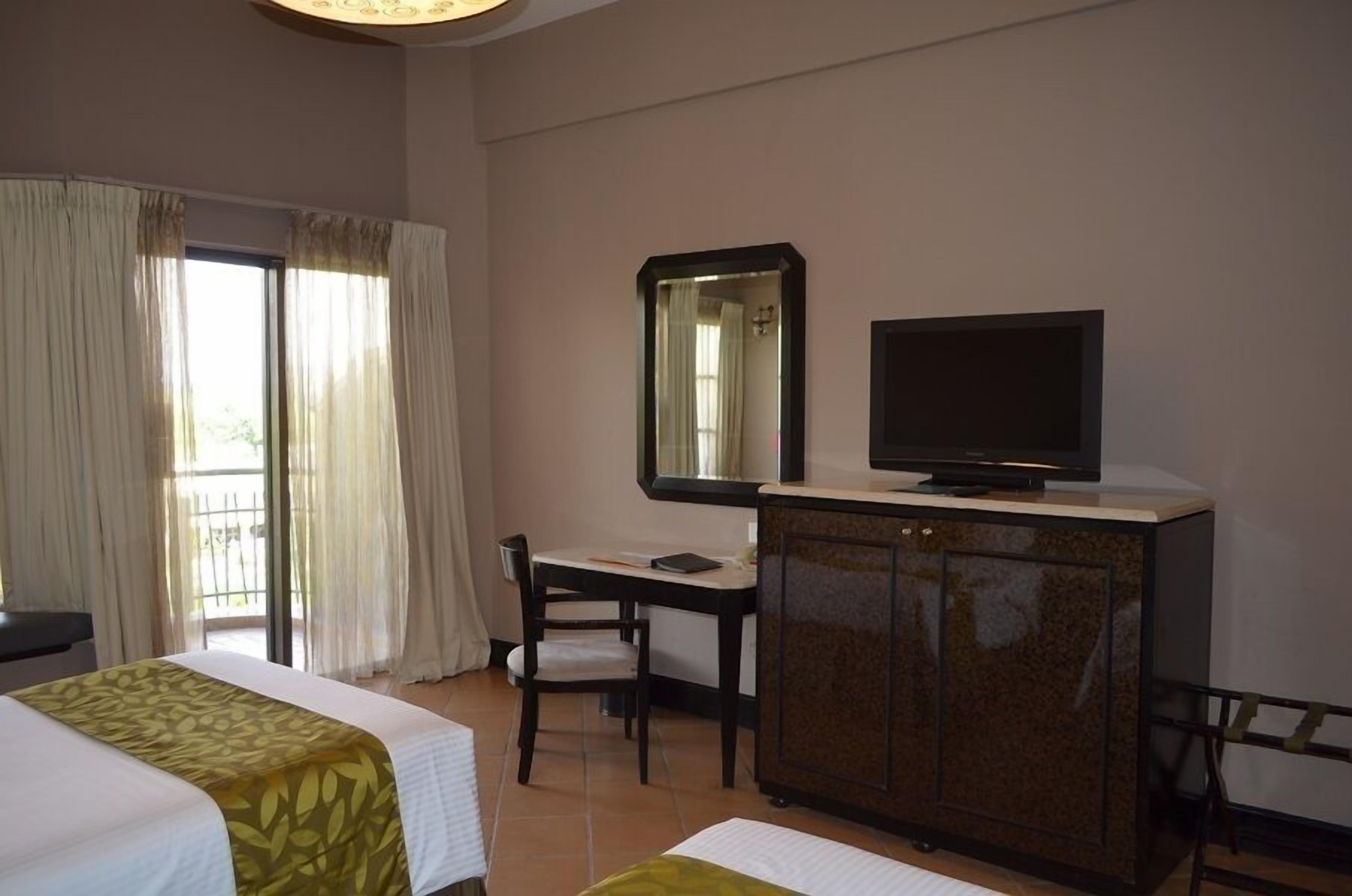 A hotel room with two beds, a desk with a chair, a television on a cabinet, and a large mirror on the wall.