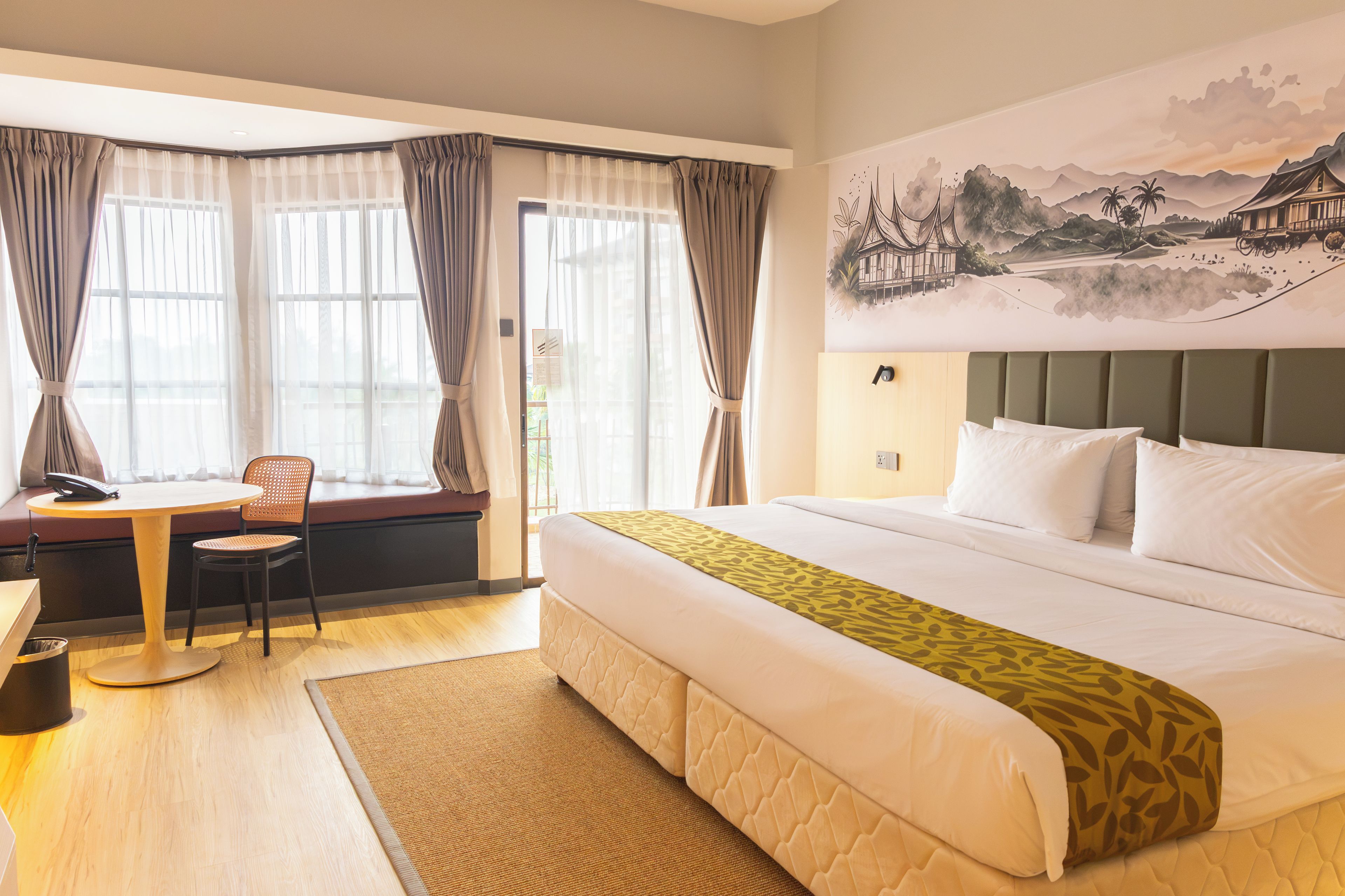 Habitación de hotel con cama, un escritorio con silla, una ventana con cortinas y un cuadro de paisaje en la pared.