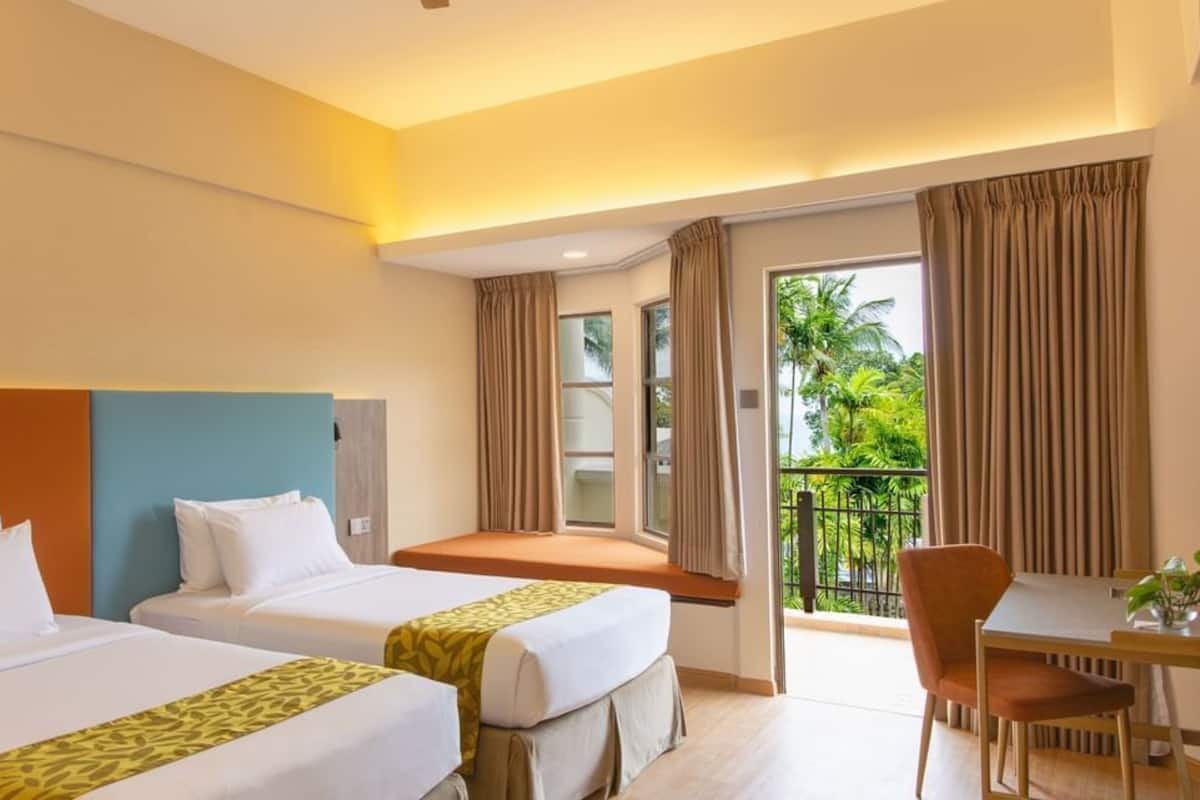 A hotel room with two beds, a balcony with curtains, a dining table, and a chair.