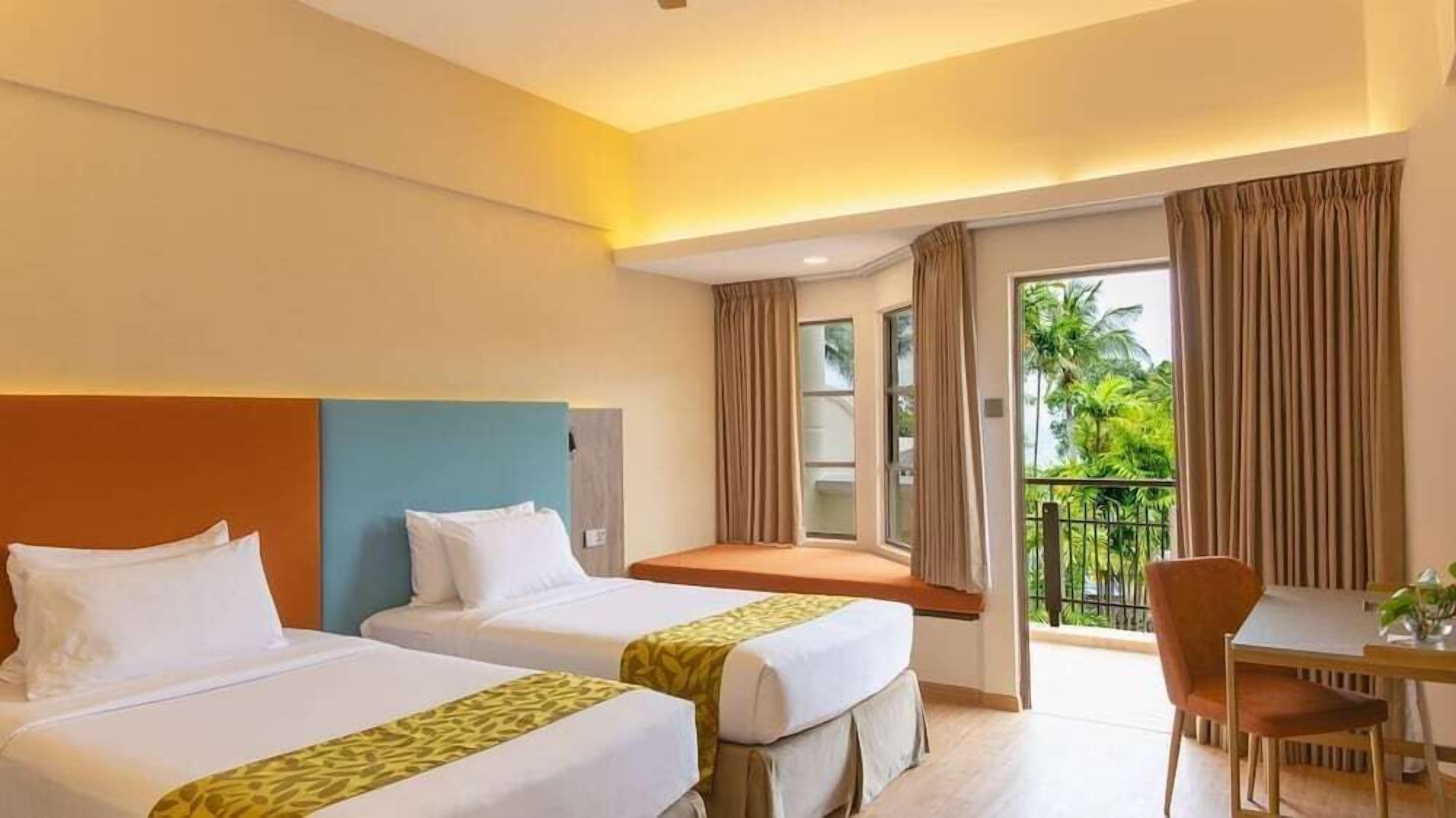 A hotel room with two beds, a balcony with curtains, a small table, and a chair.