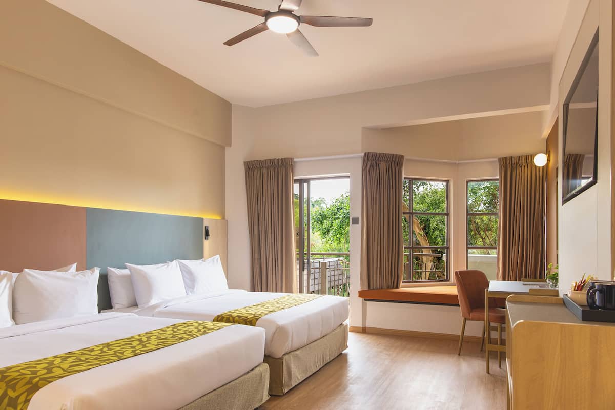 A hotel room with two beds, a desk, a chair, a ceiling fan, and a window with curtains.