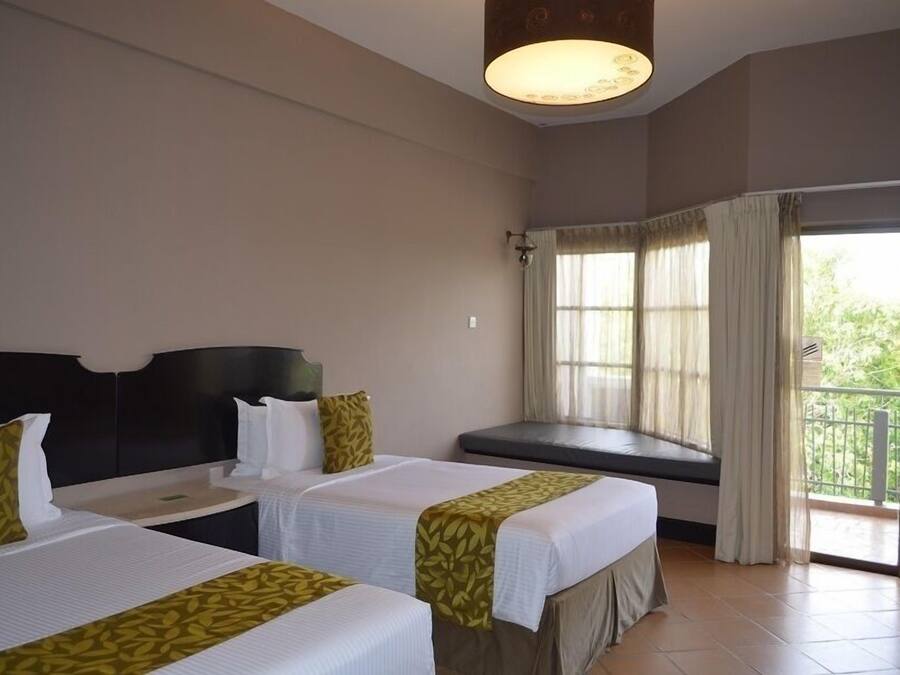 Quarto de hotel com duas camas, janela com cortinas, varanda e uma luminária no teto.