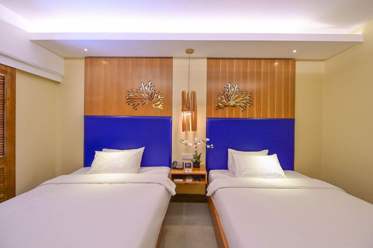Quarto de hotel com duas camas, cabeceira de madeira, parede azul decorativa e um objeto decorativo na parede.