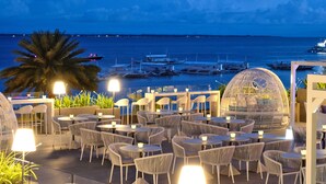 An outdoor dining area with tables and chairs, overlooking a marina with boats. - Be Resorts - Mactan (Lapu-Lapu)