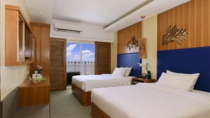 A hotel room with two beds, wooden paneling, a desk with a vase of flowers, and a view of the sky through a door. - Be Resorts - Mactan (Lapu-Lapu)