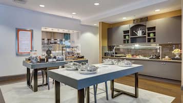 A modern breakfast area with a buffet setup, including a coffee machine, toaster, and various food items.