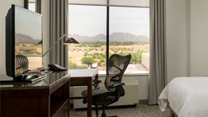 A hotel room with a desk, chair, bed, and a large window with curtains. - Hilton Garden Inn Phoenix Airport North (Phoenix)