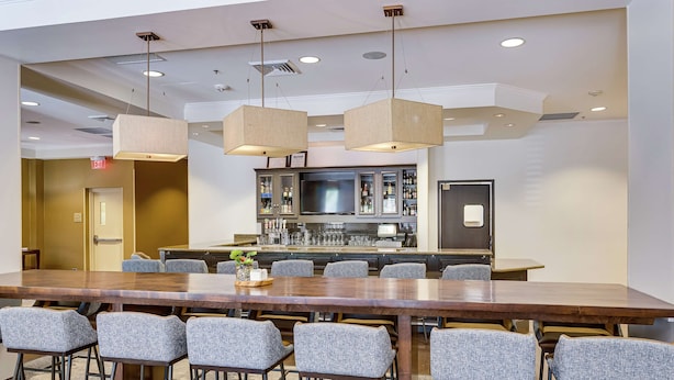 A conference room with a long table, multiple chairs, a bar area with a television, and a kitchenette. - Hilton Garden Inn Phoenix Airport North (Phoenix)