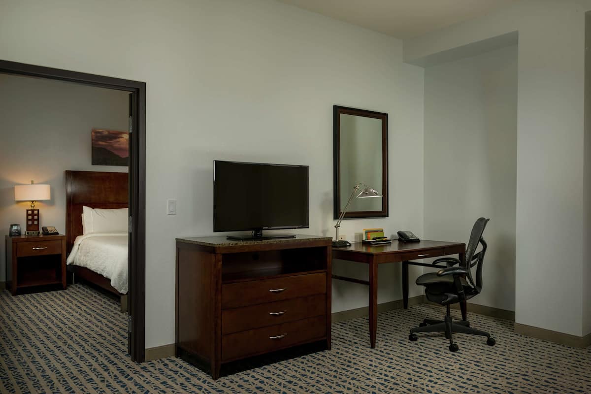 A hotel room with a bed, a desk with a computer, a TV, a chair, and a dresser.